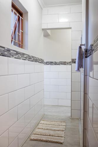 a white tiled shower with a mirror and a rug at Rock away Beach Condo. in Hartenbos