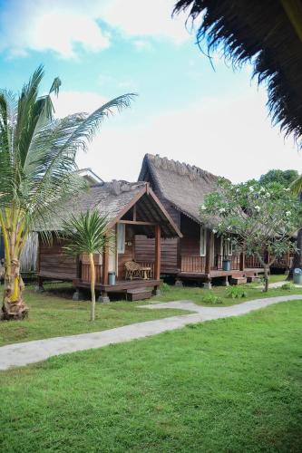 a house with a straw roof with palm trees in front at Beranda Ecolodge in Gili Air
