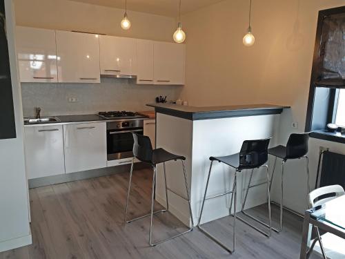 Una cocina con gabinetes blancos y encimeras y taburetes negros. en Appartment Bella - 2 minutes from the beach, en Noordwijk aan Zee