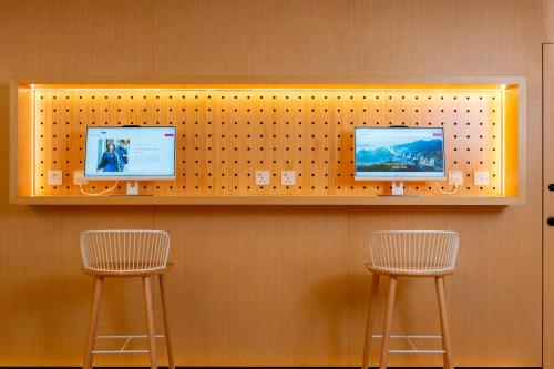 a shelf with three monitors on a wall with two chairs at Shama Hub Metro South Hong Kong in Hong Kong