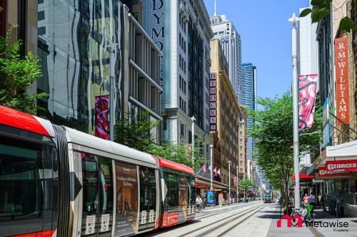 a red bus driving down a city street with buildings at MetaWise Sydney CBD Luxury City view 2BED Apartment in Sydney
