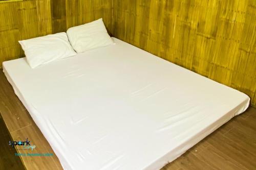 a white bed with two pillows on a wooden floor at Spark Camp - Baler Resorts in Baler