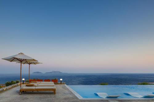 a pool with chairs and an umbrella next to the ocean at Seafront elegant villas, with infinity pools & devine views! in Agios Pavlos