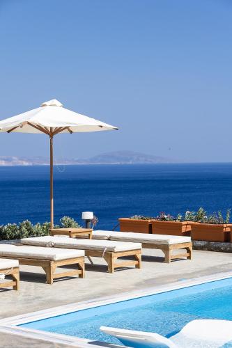 a pool with benches and an umbrella and the ocean at Seafront elegant villas, with infinity pools & devine views! in Agios Pavlos