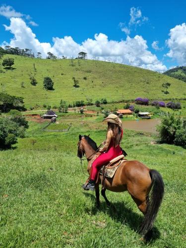 a woman sitting on a horse in a field at Chale com hidro na Serra da Mantiqueira in Sapucaí-Mirim