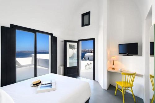 a white room with a bed and a desk and a chair at Grand Ambassador Santorini Hotel in Akrotiri
