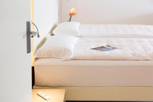 a bed with white sheets and a remote control at Hotel Vega in Malcesine