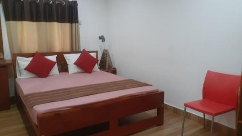 a bedroom with a bed with red pillows and a red chair at The Garden Resort Airport Katunayaka in Katunayake