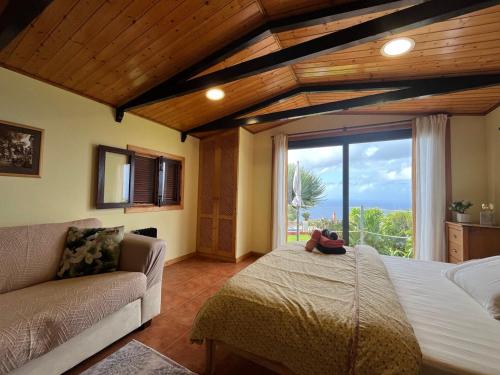 a bedroom with a bed and a couch and a large window at Ocean View Cottage in Ponta do Pargo