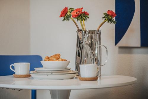 奥尔登堡LINDEN Apartment für bis zu 6 Personen mit Parkplatz, Terrasse, 2 Bäder und Babybett的一张摆着杯子的桌子和一个插着鲜花和羊角面包的花瓶