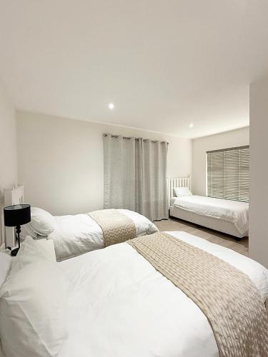 a white bedroom with two beds and a window at The Bucket List Guest House in Bredasdorp