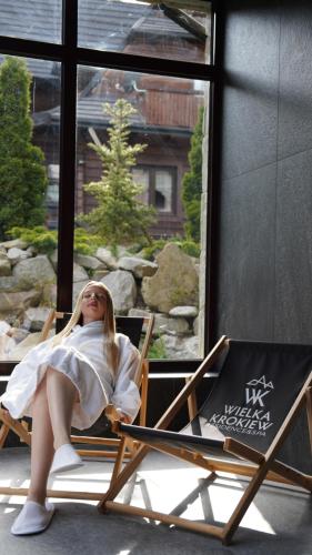 a woman sitting in a chair next to a window at Wielka Krokiew Residence&SPA - Zakopane - JACUZZI, SAUNA, TĘŻNIA SOLANKOWA, SPA, GRILL in Zakopane