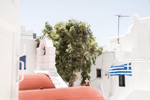 a white building with a red roof and a tree at Hotel Delfines in Mýkonos City