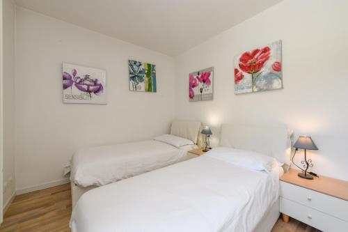two beds in a white room with pictures on the wall at Residence Rta La Rosa delle Dolomiti in Carisolo