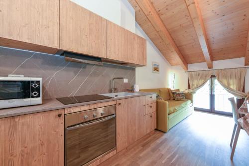 a kitchen with wooden cabinets and a microwave and a couch at Residence Rta La Rosa delle Dolomiti in Carisolo