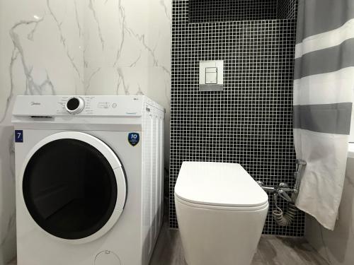 a bathroom with a white toilet and a washer at Классика Rayimbek 15-32, 1br in the centre & питьевая вода в подарок in Almaty