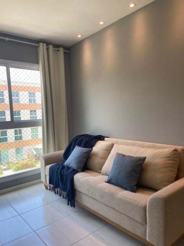 a couch with blue pillows in a room with a window at Muro Alto Condominio Club in Ipojuca