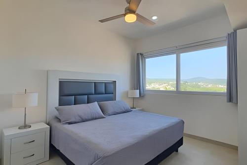 Un dormitorio con una cama con ventilador de techo y una ventana. en Costa Paraíso D-20 2-Recamaras, en Bucerías