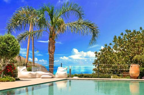 a swimming pool with chairs and palm trees and the ocean at Cretan Dream Villa in Georgioupolis