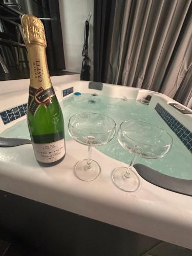 a bottle of champagne and two wine glasses on a bath tub at B&M Jacuzzi Rezidencija SELF CHECK - IN in Vilnius