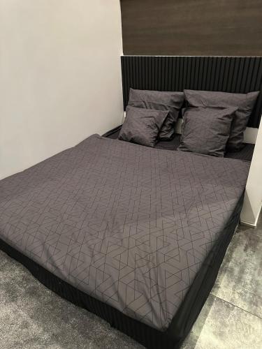 a bed with a gray comforter and pillows at B&M Jacuzzi Rezidencija SELF CHECK - IN in Vilnius