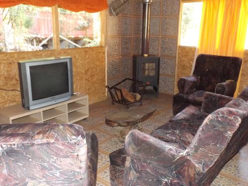 a living room with a tv and chairs and a stove at Cabañas Aguas Claras in Pinto