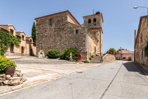 an old stone building with a clock tower on a street at Casa Rural El Viejo Almacén, a 20 minutos de Segovia in Losana de Pirón