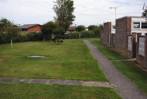 a grassy yard with a brick wall and a sidewalk at 4 Guests - Pet Friendly - Chalet Beach Home Chapel in Skegness