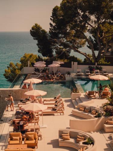 a pool with chairs and umbrellas next to the ocean at Aethos Mallorca in Paguera