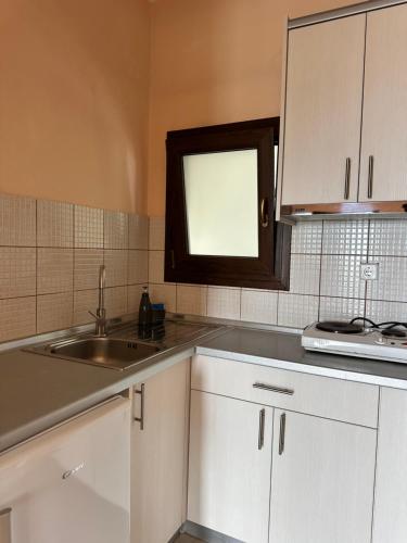 a kitchen with white cabinets and a sink and a window at Sissy's Suites San Antonio Beach Potos Thassos in Potos