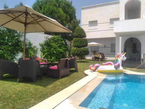 a swimming pool with chairs and an umbrella next to a house at Magnifique villa Olfa in Hammamet