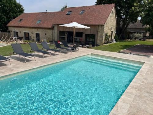 une piscine avec des chaises et un parasol ainsi qu'une maison dans l'établissement Gîte luxueux avec piscine, spa, jardin et équipements de loisirs à Sargé-lès-le-Mans - FR-1-410-437, à Sargé Les Le Mans 