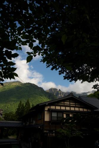 a building with mountains in the background with a tree at Minshuku Takizawa in Takayama