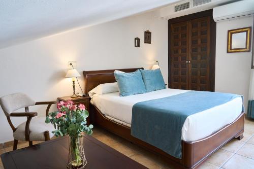 a bedroom with a bed and a chair and a vase of flowers at Hotel María de Molina in Úbeda