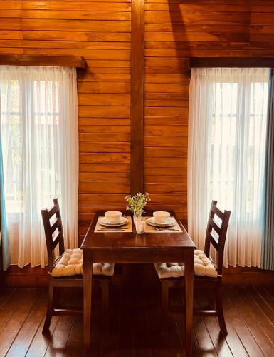 a wooden dining room table with two chairs and two windows at Sun and Moon Bungalow Village in Uluwatu