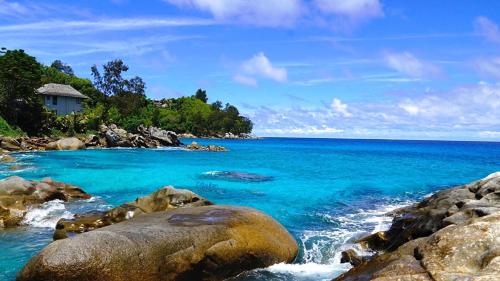 a beach with blue water and rocks and a house at Vi Miles Lodge in Mahe