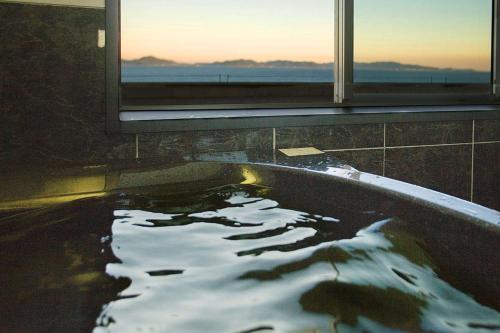 a bath tub filled with water in front of a window at Shunkeiroman Ginpaso in Gamagori