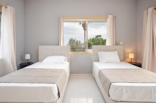 two beds in a white room with a window at Sun Wave Villa Sea View Retreat in Peyia