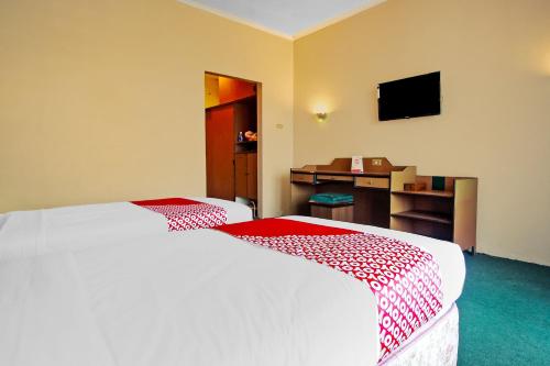 ein Schlafzimmer mit einem Bett, einem Schreibtisch und einem Fernseher in der Unterkunft OYO 2360 Hotel Rio in Bengkulu