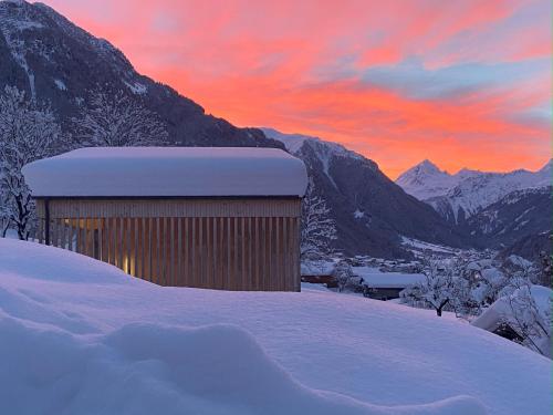 a building in the snow with a sunset in the mountains at Haus Albuin in Sankt Gallenkirch