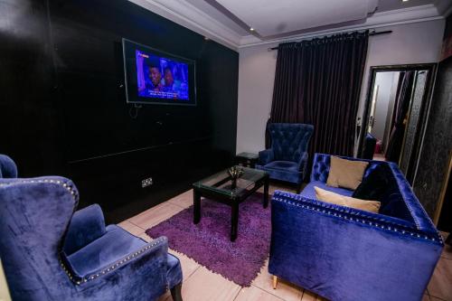 a living room with blue chairs and a tv at Elegance Suites Hotels in Lagos