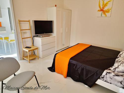 a bedroom with a bed with an orange blanket and a tv at Maison Etoile de Mer in Agnone Bagni