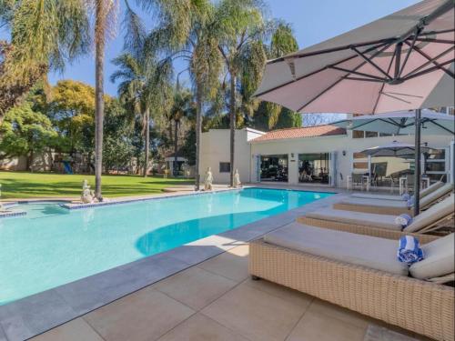 a swimming pool with chairs and an umbrella at Villa Reis - The Villa of Kings Hotel & Spa in Bedfordview
