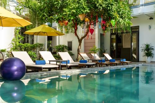 a pool with chairs and umbrellas next to a building at Blessing Villa Hoi An in Hoi An