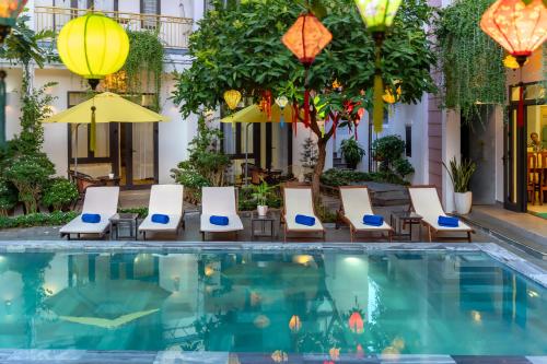 a hotel pool with chairs and umbrellas at Blessing Villa Hoi An in Hoi An