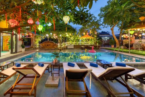 a pool with tables and chairs in front of it at Blessing Villa Hoi An in Hoi An