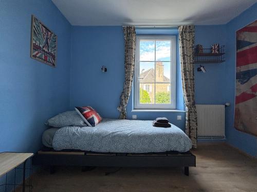 a blue bedroom with a bed and a window at Les continents maison spacieuse 4 belles chambres parking privatif terrasse à 5 mn à pied tous commerces et 20 mn plage Omaha Beach et à 15 mn de Bayeux in Le Molay-Littry