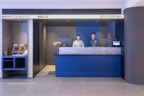 two people standing at a counter in a lobby at Atour Light Hotel Shandong University Central Campus in Jinan