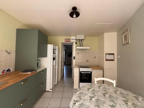 a kitchen with a table and a white refrigerator at Les continents maison spacieuse 4 belles chambres parking privatif terrasse à 5 mn à pied tous commerces et 20 mn plage Omaha Beach et à 15 mn de Bayeux in Le Molay-Littry