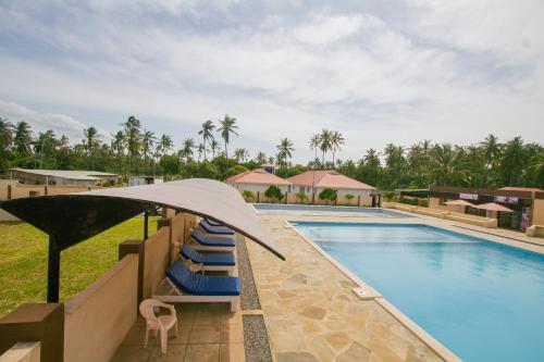 a pool at a resort with lounge chairs and an umbrella at Havillah Gardens Watamu in Watamu